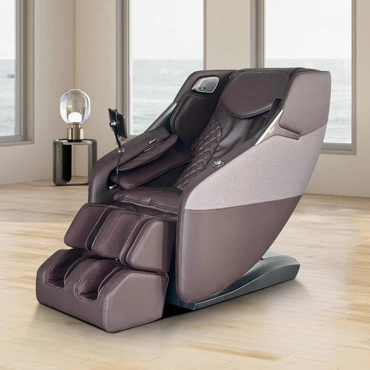 Brown Titan Pro 4D Astro massage chair in a sunlit living room with ocean-view windows