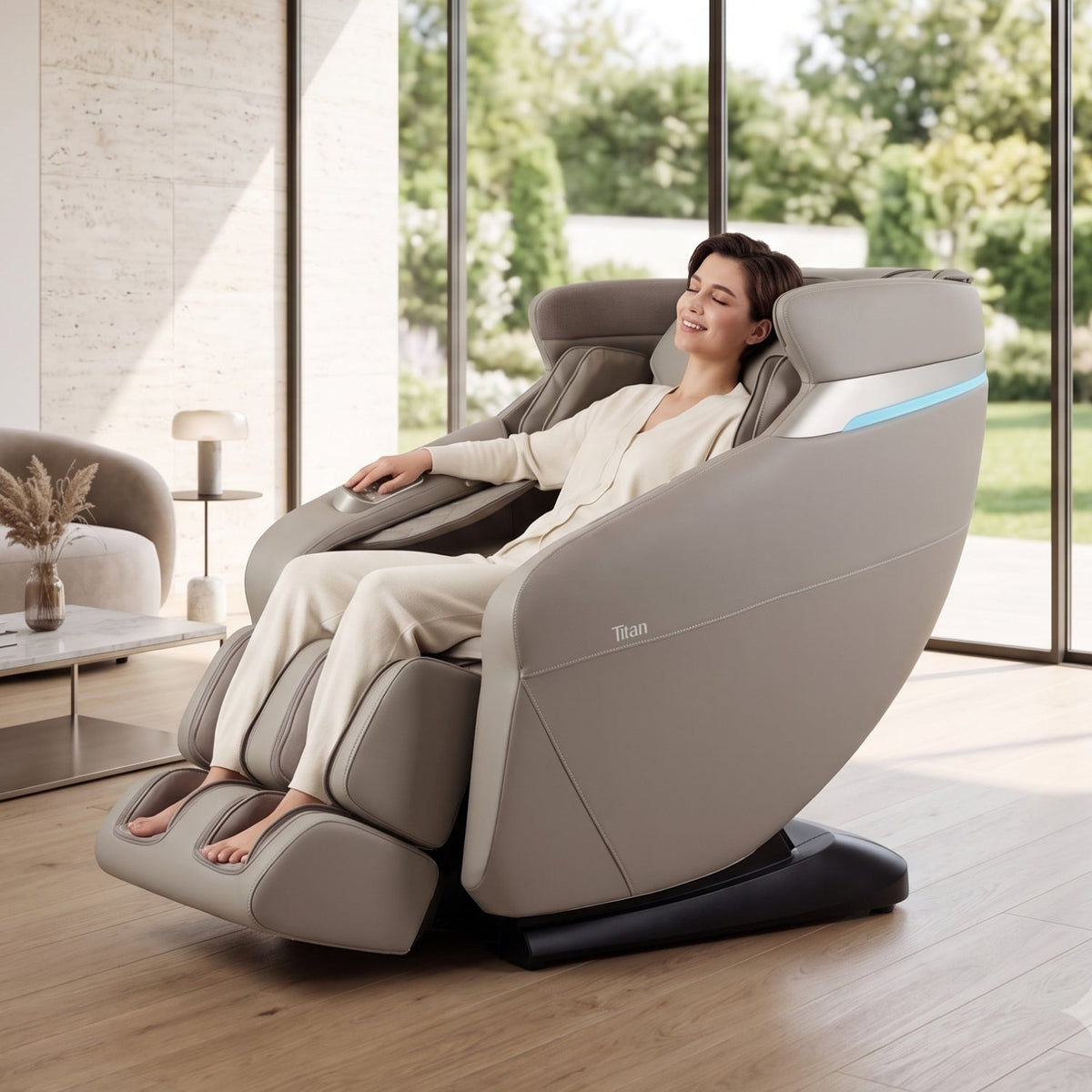 Woman relaxing in a Taupe Titan Forma 3D+2D massage chair in a bright living room with garden windows
